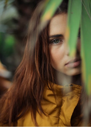 A young woman in mustard coloured raincoat looking straight at the camera.