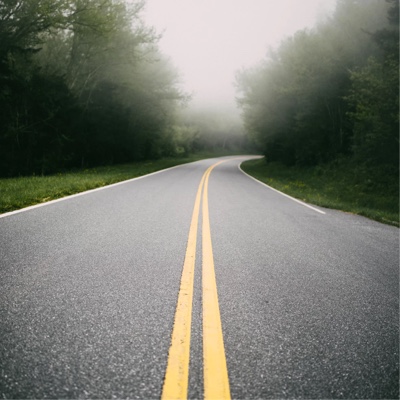 A clear two-way road with trees on both sides and a bit of fog up ahead.